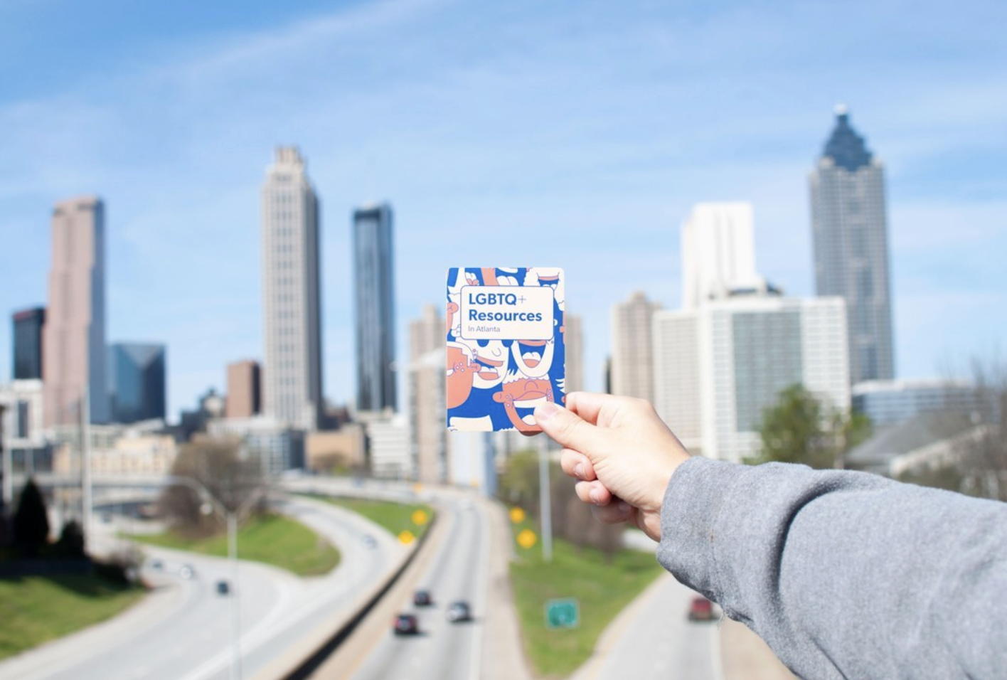 Hand holding LGBTQ+ Resources In Atlanta pocket guide with the Atlanta skyline in the background